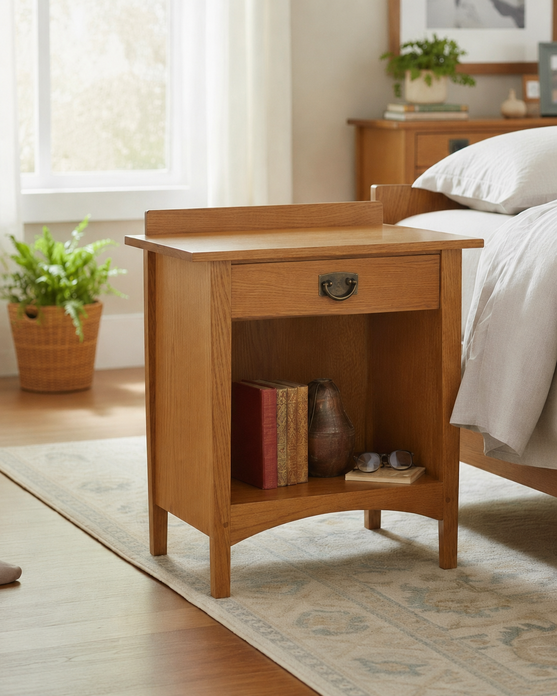 Enclosed Shelf Nightstand in solid oak with antique brass ring pull, single drawer, open lower shelf, and arched apron base, styled beside a bed in a light-filled bedroom

